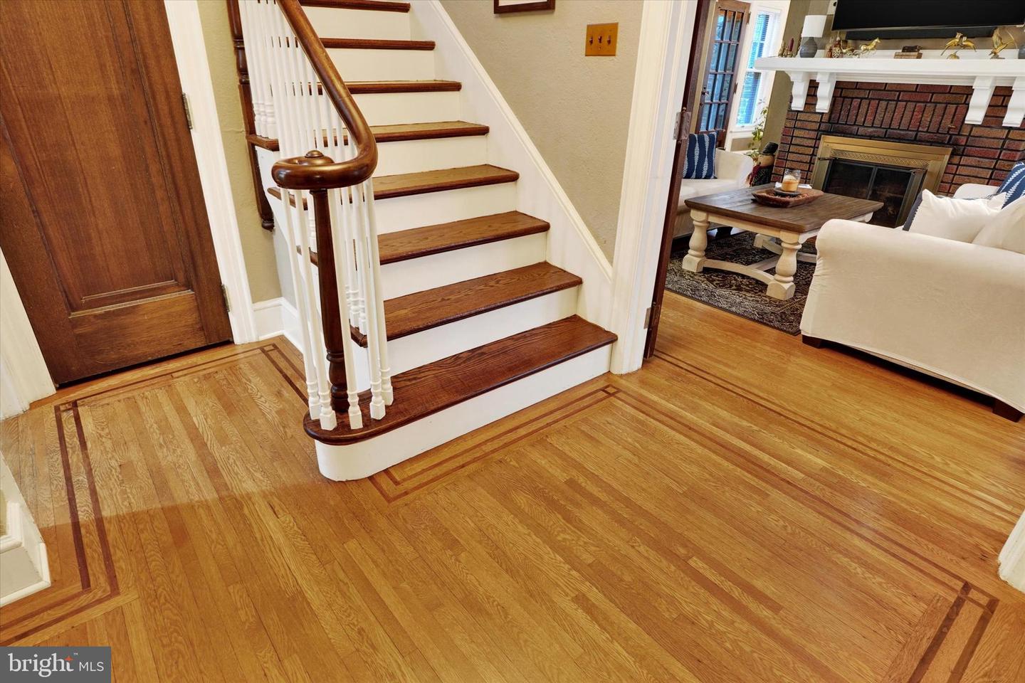 Main staircase at 185 Peyton Road with original hardwood floors featuring decorative inlaid border, newel post, and view into living room