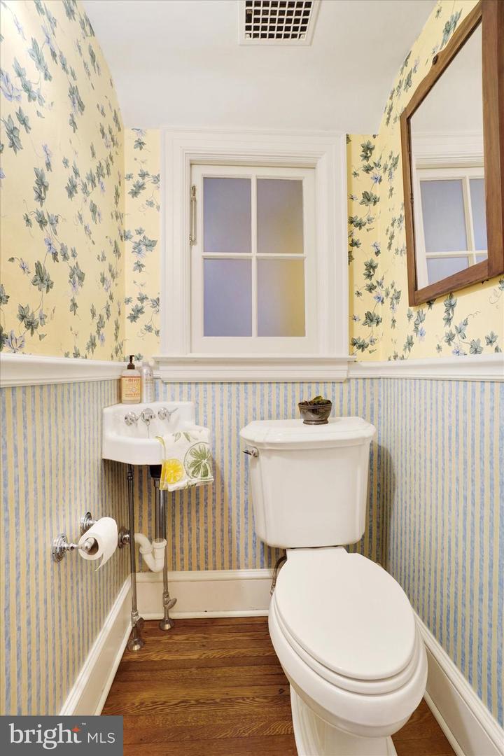 First-floor powder room at 185 Peyton Road with vintage corner sink, floral wallpaper, and hardwood floors