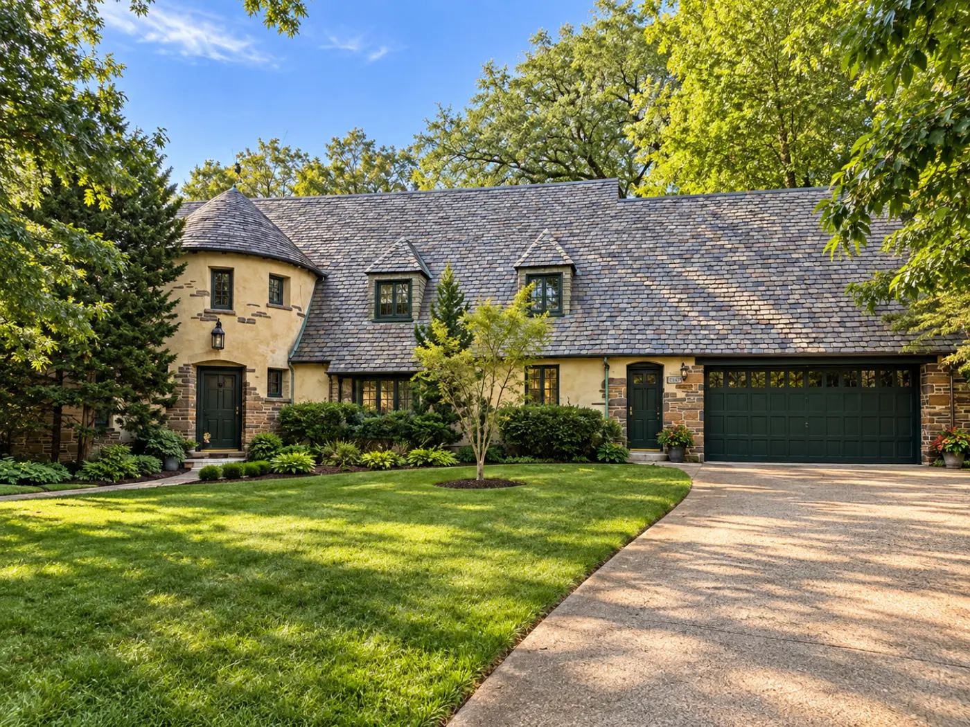 A stucco and stone house with a round tower under a conical roof, an arched door, dormers and a variegated slate roof