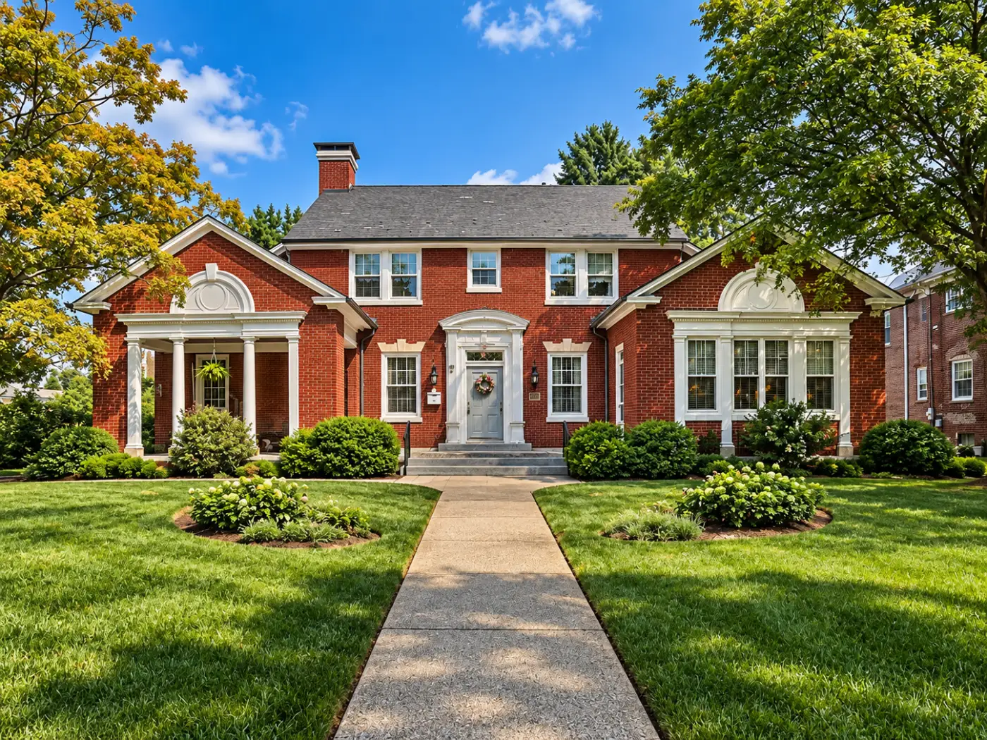 A red brick Colonial Revival house with a columned side porch and bay windows under broken pediments