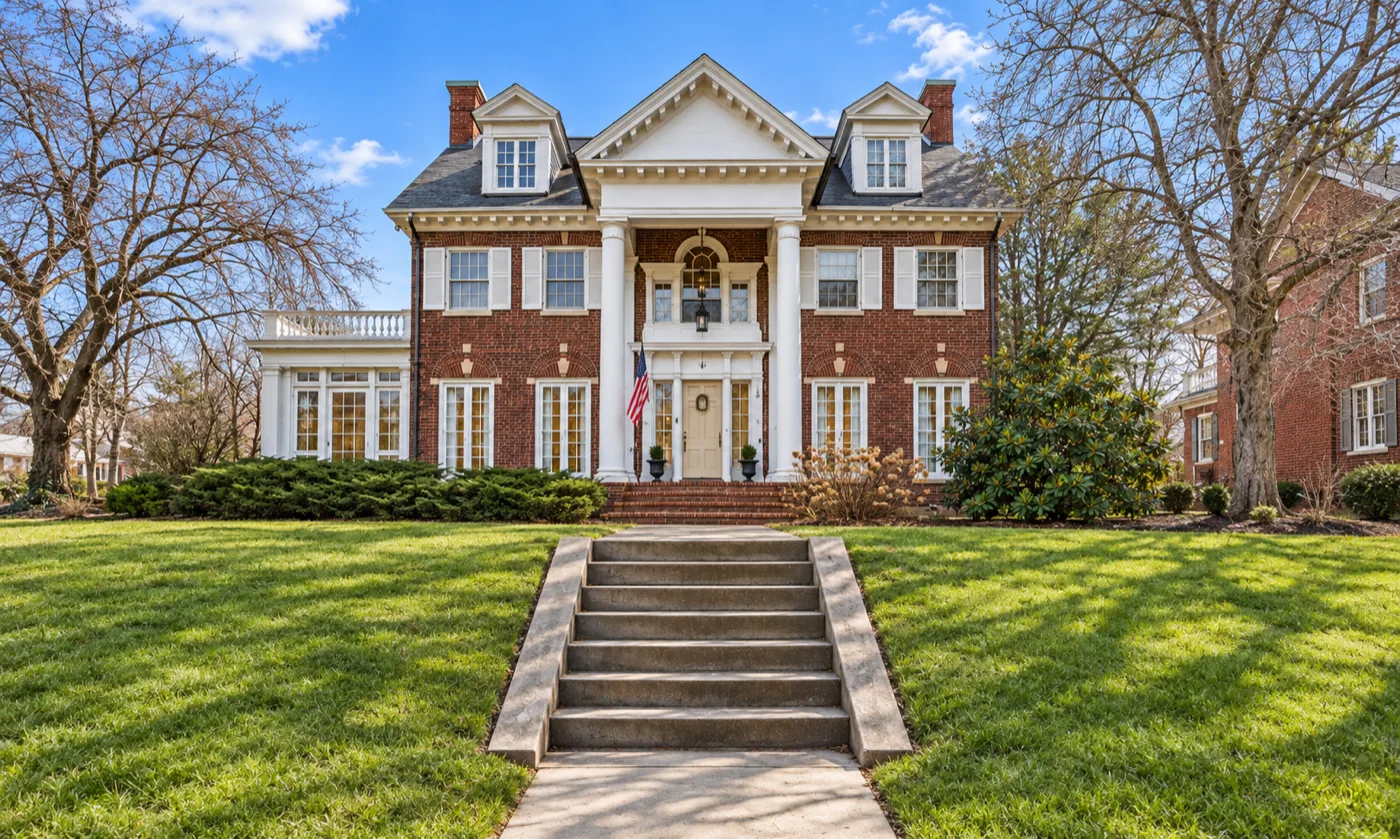 A red brick house behind a two-storey portico on tall white columns, a pedimented gable above and a dormer to each side